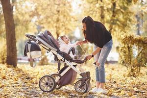 madre con ropa informal con su hijo en cochecito está en el hermoso parque de otoño foto