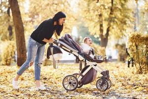 madre con ropa informal con su hijo en cochecito está en el hermoso parque de otoño foto