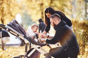 familia alegre divirtiéndose junto con su hijo en un cochecito en un hermoso parque de otoño foto