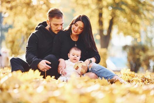 Cheerful family sits on the ground and having fun together with their child in beautiful autumn park photo