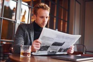 Portrait of modern young guy in formal clothes that sits in the cafe and reads newspaper photo