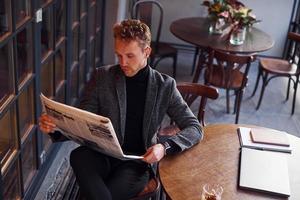 Portrait of modern young guy in formal clothes that sits in the cafe and reads newspaper photo