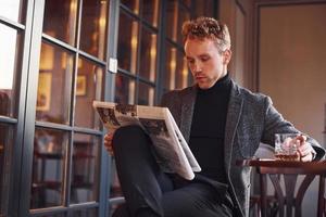 Portrait of modern young guy in formal clothes that sits in the cafe and reads newspaper photo