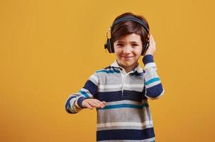 Cute little boy with headphones in the studio against yellow background photo