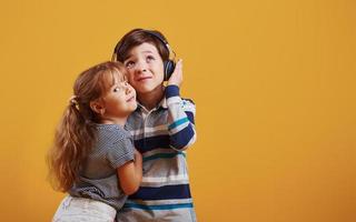 Little girl with boy stands together in the studio against yellow background photo