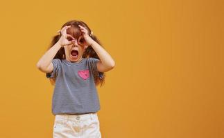 Cute little girl in casual clothes have fun in the studio against yellow background photo