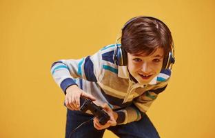 Cute little boy playing video game in the studio against yellow background photo