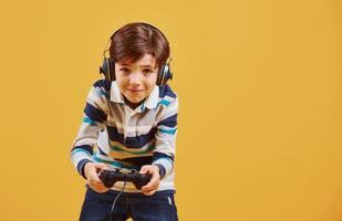 Cute little boy playing video game in the studio against yellow background photo