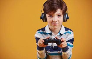 Cute little boy playing video game in the studio against yellow background photo