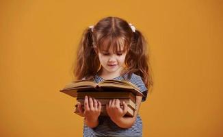 Cute little girl with book in hands in the studio against yellow background photo