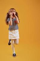 Cute little girl in casual clothes have fun in the studio against yellow background photo