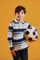 retrato de joven futbolista con balón. se encuentra contra el fondo amarillo foto