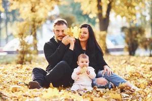 la familia alegre se sienta en el suelo y se divierte junto con su hijo en el hermoso parque de otoño foto