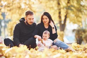 la familia alegre se sienta en el suelo y se divierte junto con su hijo en el hermoso parque de otoño foto