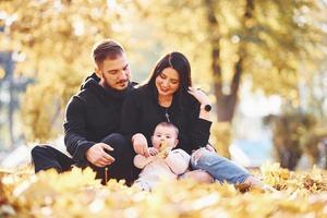 la familia alegre se sienta en el suelo y se divierte junto con su hijo en el hermoso parque de otoño foto