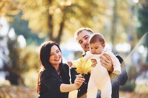 Cheerful family having fun together with their child in beautiful autumn park photo