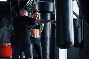 joven entrenador de boxeo tatuado enseña a mujer joven en el gimnasio foto