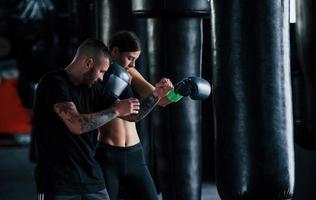 joven entrenador de boxeo tatuado enseña a mujer joven en el gimnasio