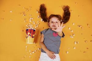 Cute little girl with popcorn lying down on the yellow floor photo