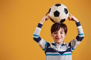 retrato de joven futbolista con balón. se encuentra contra el fondo amarillo foto