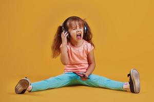 retrato de una linda niñita con auriculares y teléfono en el estudio con fondo amarillo foto