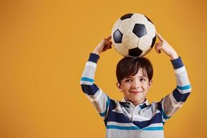 retrato de joven futbolista con balón. se encuentra contra el fondo amarillo foto