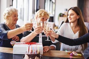 golpeando vasos. mujer mayor con familiares y amigos celebrando un cumpleaños en el interior foto