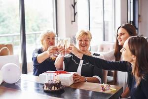 golpeando vasos. mujer mayor con familiares y amigos celebrando un cumpleaños en el interior foto