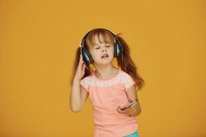 retrato de una linda niñita con auriculares y teléfono en el estudio con fondo amarillo foto