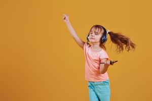 retrato de una linda niñita con auriculares y teléfono en el estudio con fondo amarillo foto