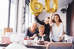 globos con el número 60. mujer mayor con familiares y amigos celebrando un cumpleaños en el interior foto