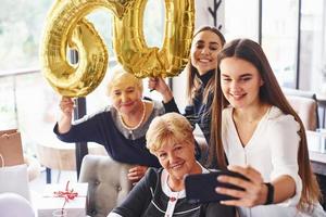 globos con el número 60. mujer mayor con familiares y amigos celebrando un cumpleaños en el interior foto