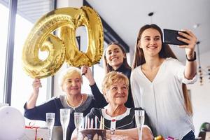 globos con el número 60. mujer mayor con familiares y amigos celebrando un cumpleaños en el interior foto