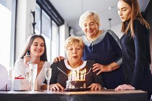 soplando las velas. mujer mayor con familiares y amigos celebrando un cumpleaños en el interior foto