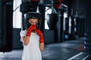 Young little girl in sportive wear and protective hat is in the gym have exercise day. Conception of boxing photo