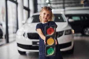 Portrait of cute little girl that holds traffic lights picture in hands in automobile salon photo