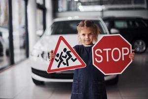 Portrait of cute little girl that holds road signs in hands in automobile salon photo