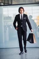 Portrait of handsome young businessman in black suit and tie and with shopping bag photo