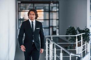 Portrait of handsome young businessman in black suit and tie walks indoors photo