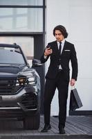 Portrait of handsome young businessman in black suit and tie outdoors near modern car photo