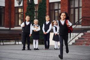 Group of kids in school uniform posing to the camera outdoors together near education building photo