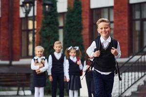 Group of kids in school uniform posing to the camera outdoors together near education building photo