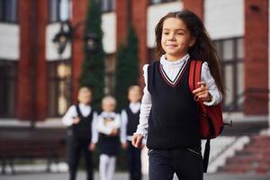 grupo de niños con uniforme escolar posando juntos para la cámara al aire libre cerca del edificio educativo foto