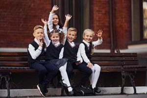 grupo de niños con uniforme escolar que están juntos al aire libre cerca del edificio de educación