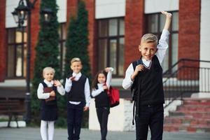 Group of kids in school uniform posing to the camera outdoors together near education building photo