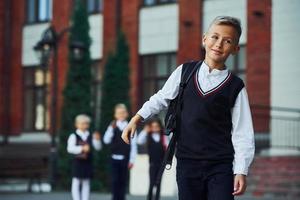 Group of kids in school uniform posing to the camera outdoors together near education building photo