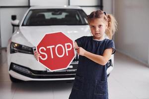 Portrait of cute little girl that holds road sign in hands in automobile salon photo