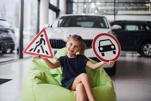 Portrait of cute little girl that holds road signs in hands in automobile salon photo