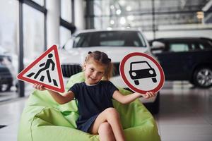 Portrait of cute little girl that holds road signs in hands in automobile salon photo