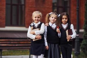 grupo de niñas con uniforme escolar que están juntas al aire libre cerca del edificio de educación foto